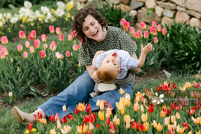 妈妈在郁金香花园的草地上和蹒跚学步的儿子玩耍图片素材