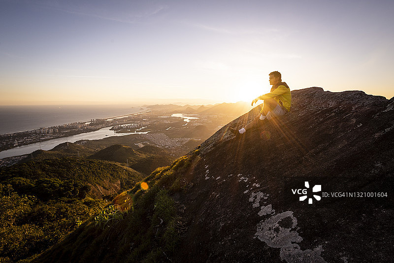 坐在岩石山边欣赏美丽日落景观的男人图片素材
