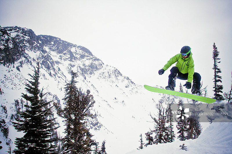 滑雪板爱好者在雪地跳跃后身穿绿色服装在空中图片素材