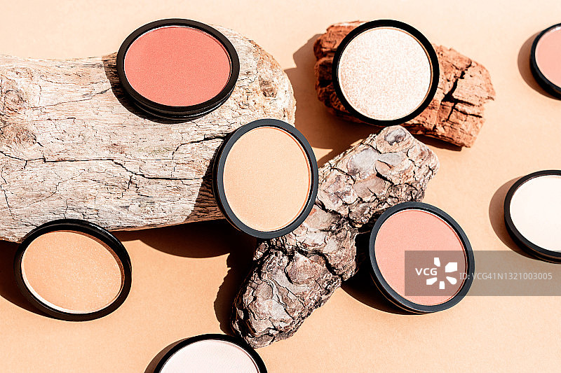 米色背景上的粉饼、腮红、眼影和木块，用于轮廓塑造的化妆品图片素材