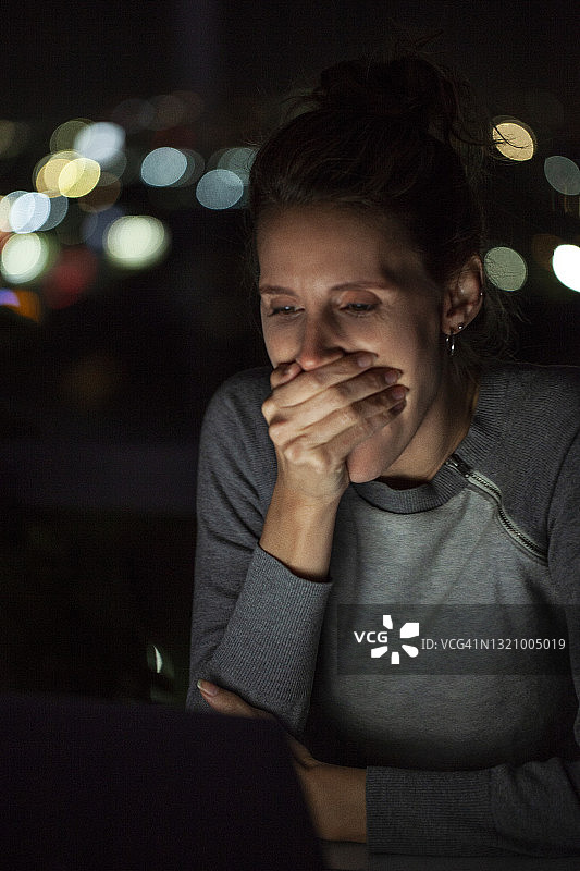 中年妇女在夜晚使用笔记本电脑时打哈欠图片素材