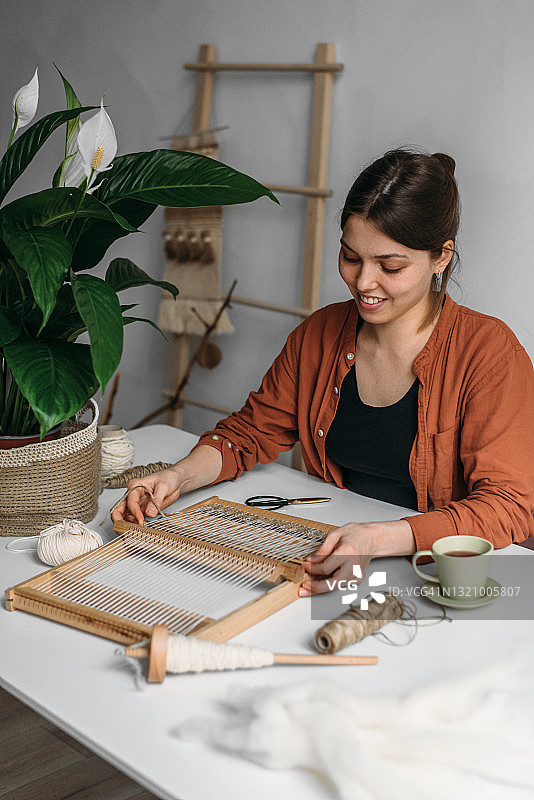 微笑的女人在桌旁编织羊毛地毯图片素材