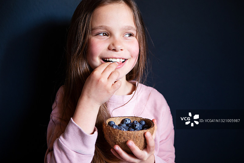 微笑的女孩在深色背景下采摘新鲜蓝莓图片素材