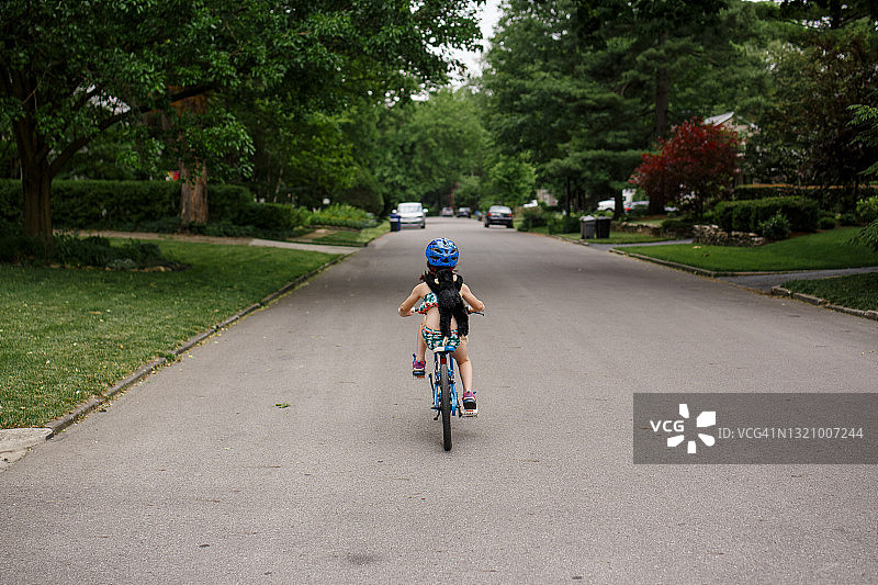 小女孩独自骑自行车，后座带着玩具猴子图片素材