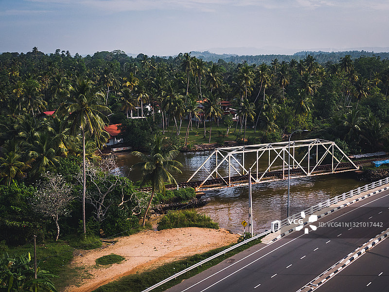斯里兰卡棕榈树环绕的河流上的道路和铁路桥梁鸟瞰图图片素材