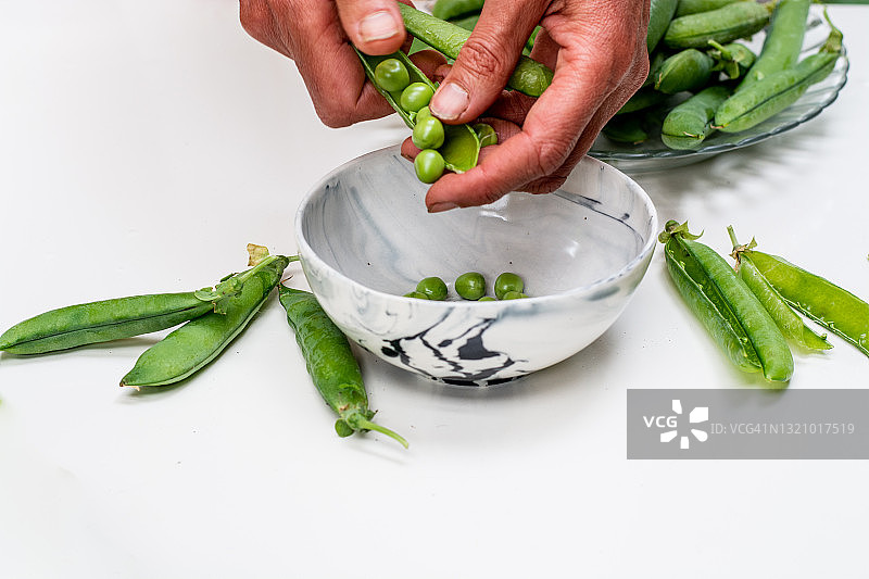 在厨房里，女人的手在碗里剥新鲜的豌豆特写图片素材