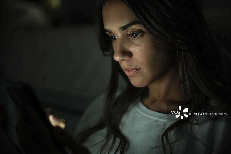 在黑暗中拿着手机看屏幕的年轻女子肖像图片素材