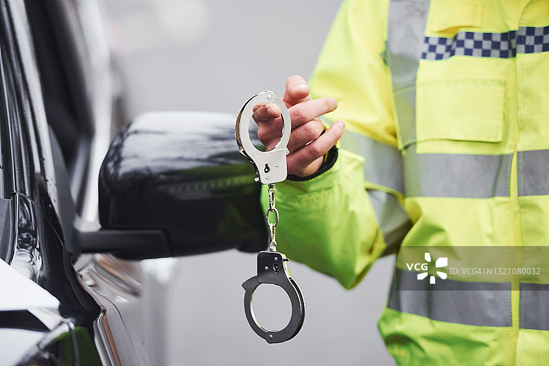 身穿绿色制服、手持手铐站在汽车旁的男警官图片素材