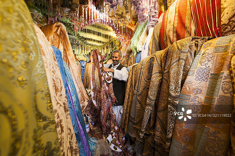 男人站在喀布尔市场里一堆五颜六色的布料中图片素材