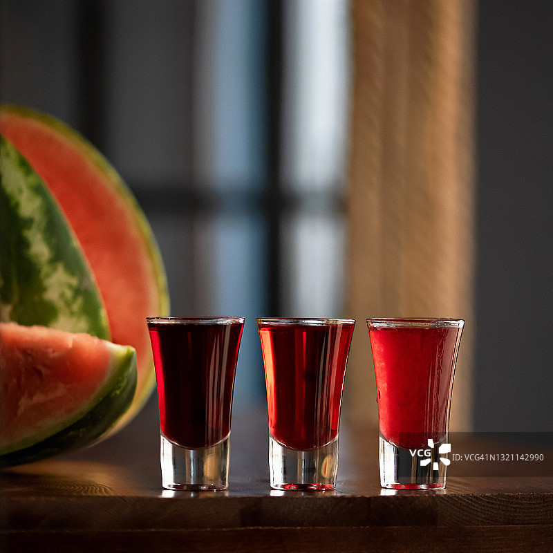 三杯矮酒精饮品。桌上的红色鸡尾酒或饮品，配有西瓜。模糊的背景。在图像顶部复制文本空间图片素材