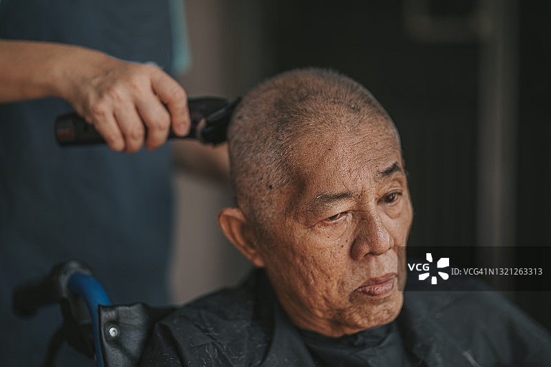 中国老年男子坐在轮椅上在家门口理发图片素材