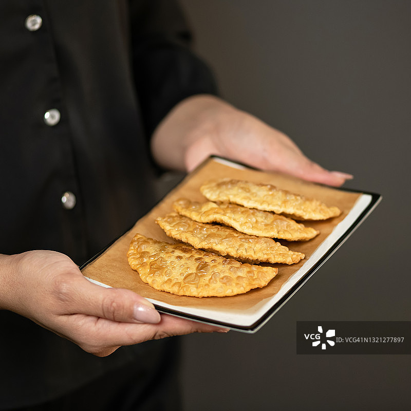 女厨师拿着一盘放在烤纸上的新鲜炸肉馅卷饼。美味的肉馅油炸馅饼，酥脆的酥皮点心，特写镜头。柔焦。垃圾食品。留白图片素材
