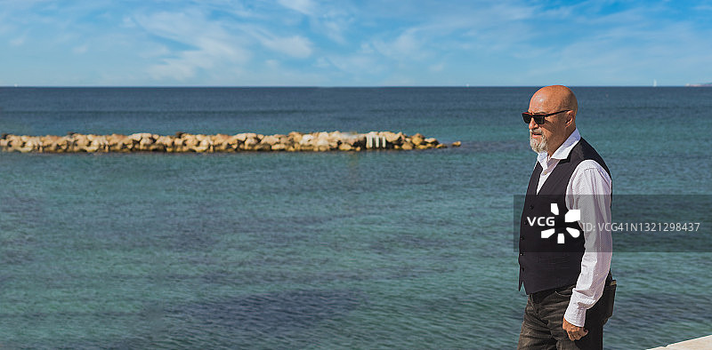 在海边散步的山羊胡中年秃顶男人，留白图片素材