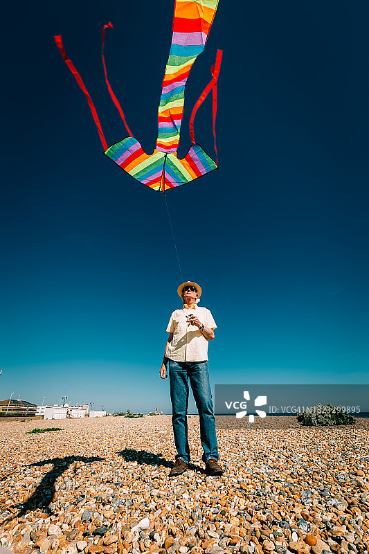 年长的男人在海滩上放飞彩色彩虹风筝图片素材