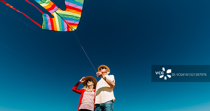 老年夫妇在海滩放飞彩色彩虹风筝图片素材