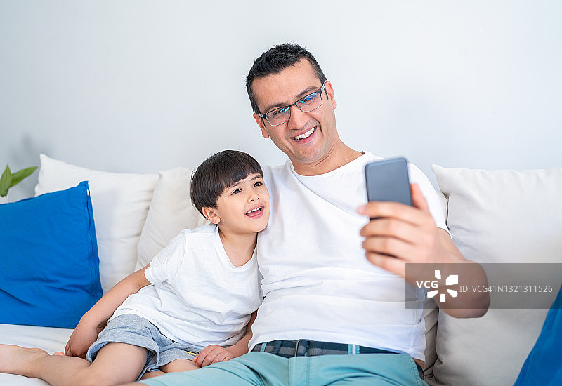 快乐的父子在家用手机观看卡通视频图片素材