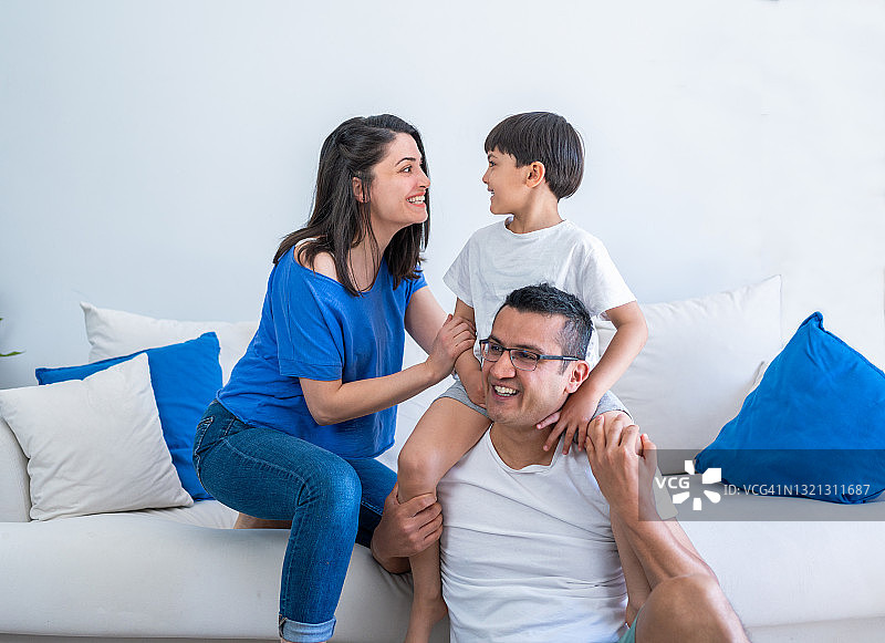 幸福家庭在家中享受欢乐时光：父母和儿子在现代客厅里放松身心，玩耍图片素材