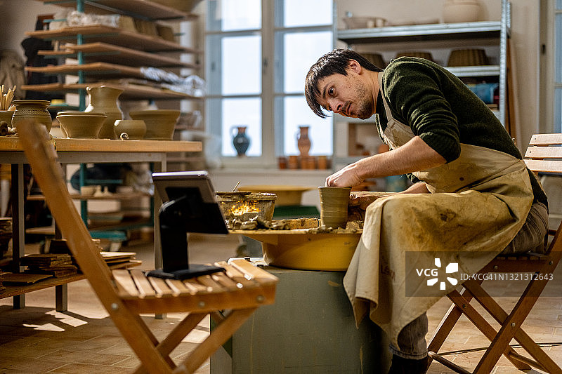 男人在工作室观看视频教程并制作陶罐图片素材