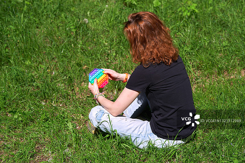 女人坐在草地上玩指尖玩具，新款时尚硅胶抗压玩具图片素材