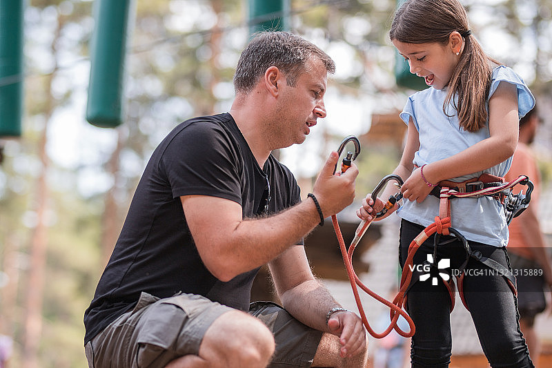 快乐的女孩在游乐园里让父亲帮她系腰带图片素材