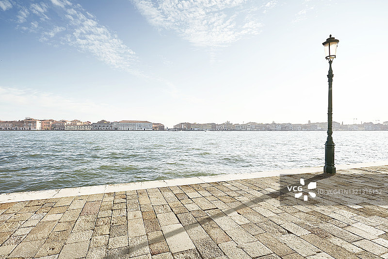 阳光明媚的日子里，平静水面附近的空旷大型走道图片素材