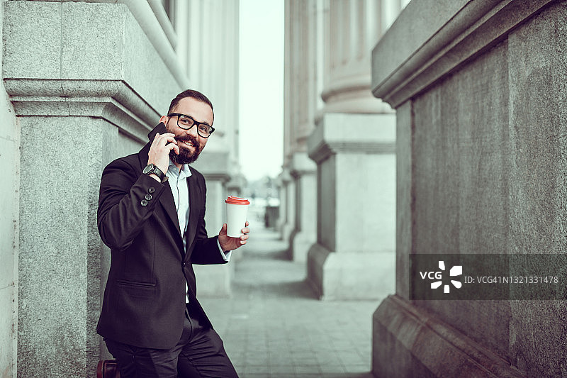 微笑的络腮胡商人享受着电话和美味的外卖咖啡图片素材