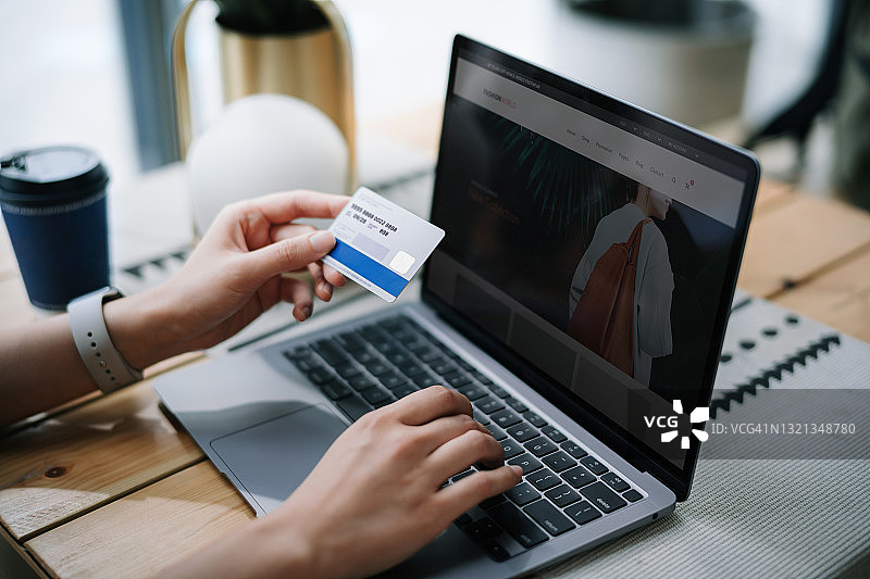 年轻女子在咖啡馆放松，使用笔记本电脑在线购物并通过信用卡进行移动支付的局部照片。生活方式与科技，舒适快捷的在线购物体验图片素材