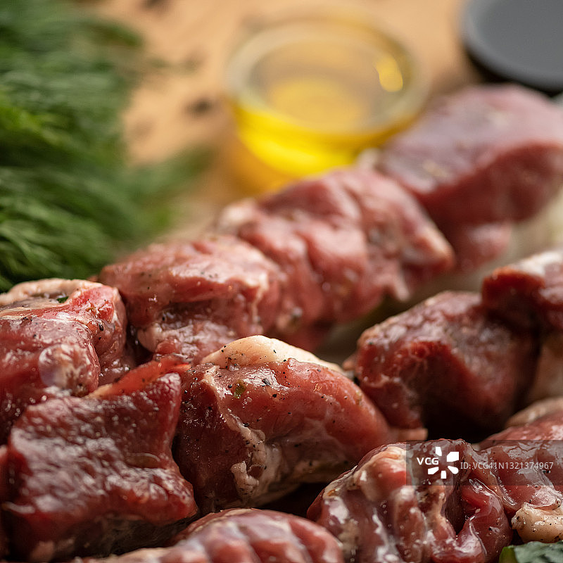 腌制生肉准备在烤肉串上烘烤。烤肉串的准备和烹饪过程。西冷牛排、香料和蔬菜在厨房的桌子上。模糊的背景。特写镜头。柔焦。正方形构图图片素材
