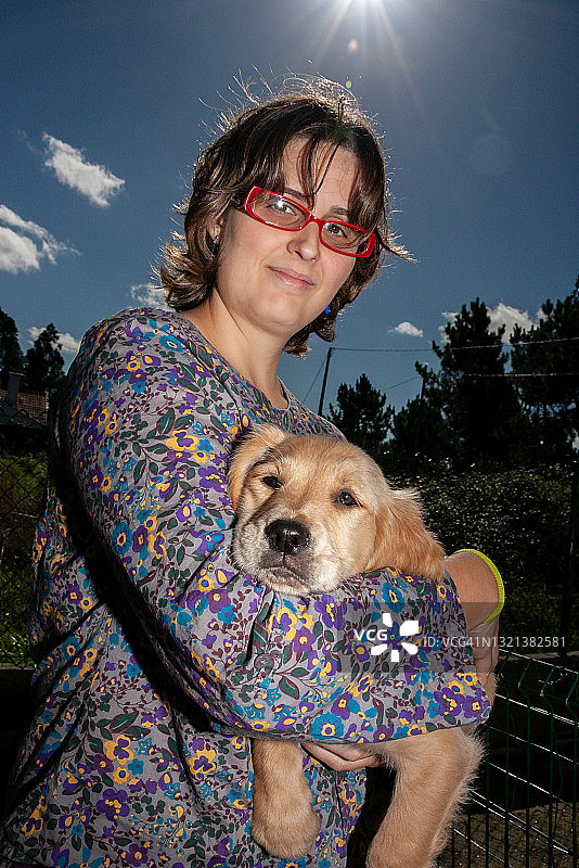 阳光明媚的日子里，中年女人在公园里抱着小金毛巡回猎犬图片素材