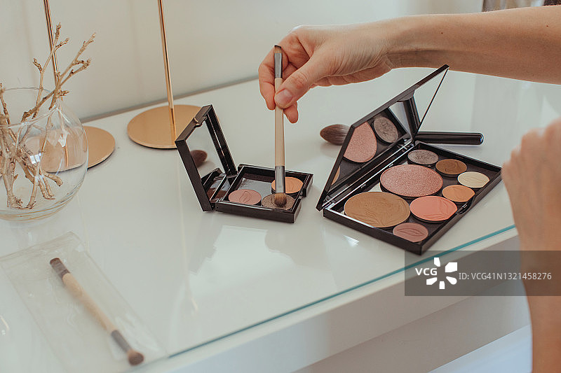 在梳妆台上，女人的手将化妆刷浸入化妆盘的特写图片素材