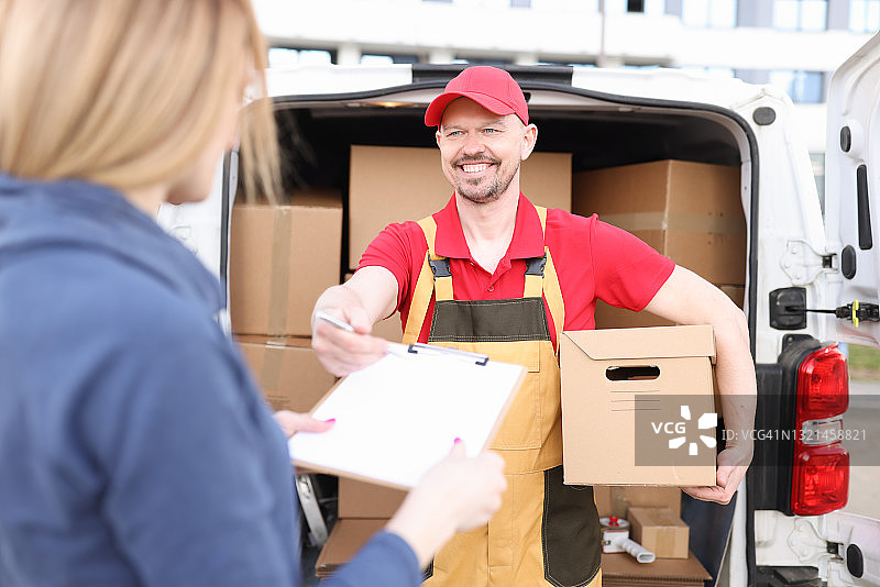 面带微笑的男快递员将带笔的剪贴板交给女士签收包裹图片素材