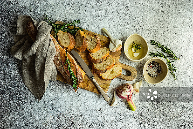 法棍切片面包与橄榄油、大蒜、盐、胡椒和迷迭香的俯视图图片素材