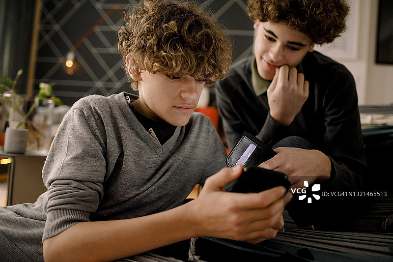 男孩们在客厅里看哥哥使用的智能手机图片素材