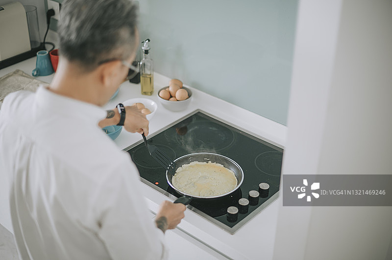 清晨，中国亚洲老人用煎锅在厨房煎鸡蛋准备早餐图片素材