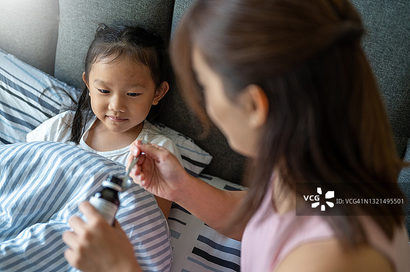 亚洲妈妈给女儿喂止咳糖浆图片素材