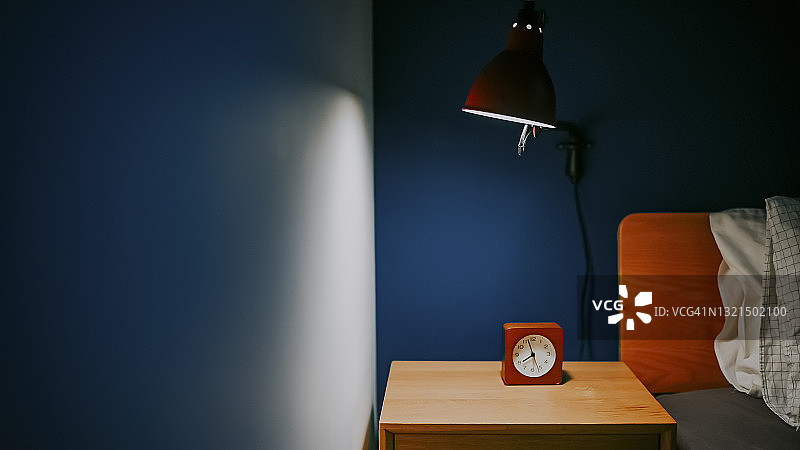 夜晚电灯照亮的卧室，床边桌上有时钟，蓝色墙壁图片素材