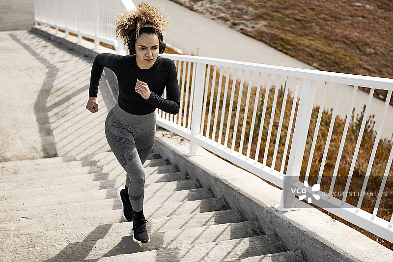 年轻女人在城市环境中戴着耳机跑步图片素材