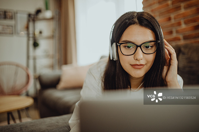 坐在沙发上用笔记本电脑耳机学习的年轻女学生图片素材