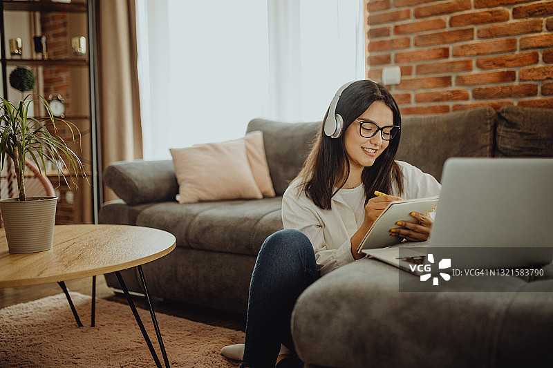 坐在沙发上用笔记本电脑耳机学习的年轻女学生图片素材