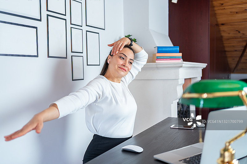 年轻女人在家中办公室的笔记本电脑前做运动和伸展运动图片素材