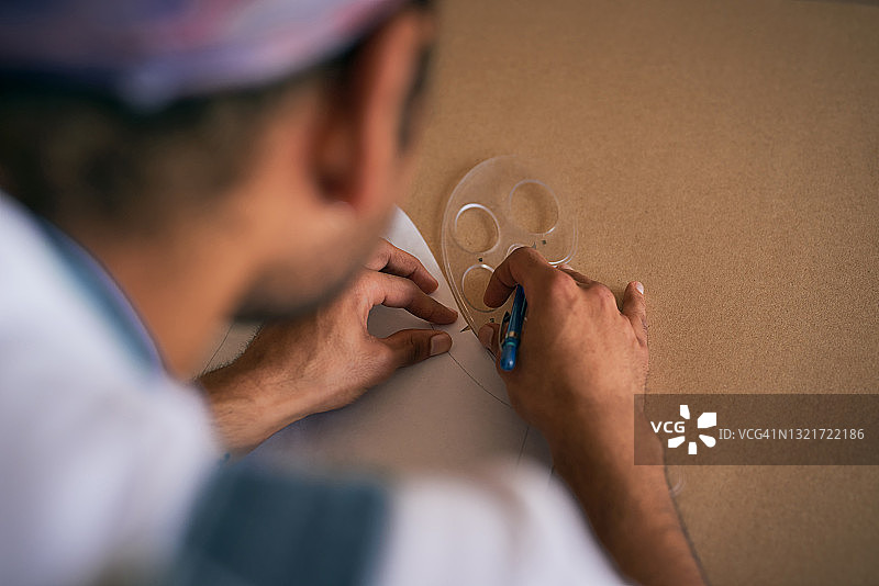 工作室里，独自站立的裁缝在纸板上绘制图案的局部照片图片素材