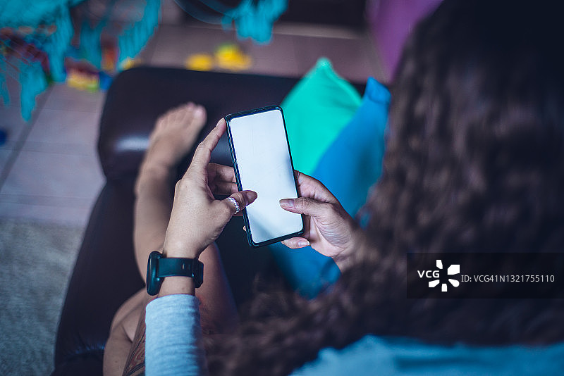 年轻女子在家中沙发上使用智能手机的照片图片素材