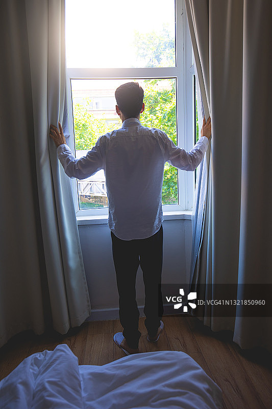 清晨，年轻男子拉开窗帘图片素材