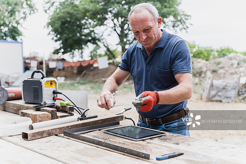 在非城市地区的工作台上工作并阅读数字平板电脑上的说明的工人图片素材