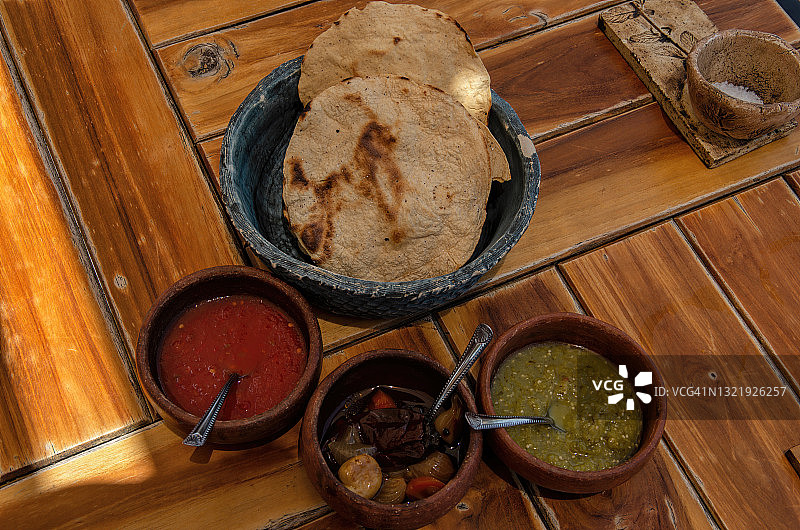墨西哥玉米饼和调味碗，包括红辣椒酱、油腌烤蔬菜和绿色沙司，放在木制户外桌子上图片素材