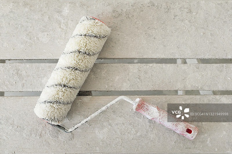 木桌或梯子上沾满白色油漆的建筑滚筒，房屋建造或公寓维修工具图片素材