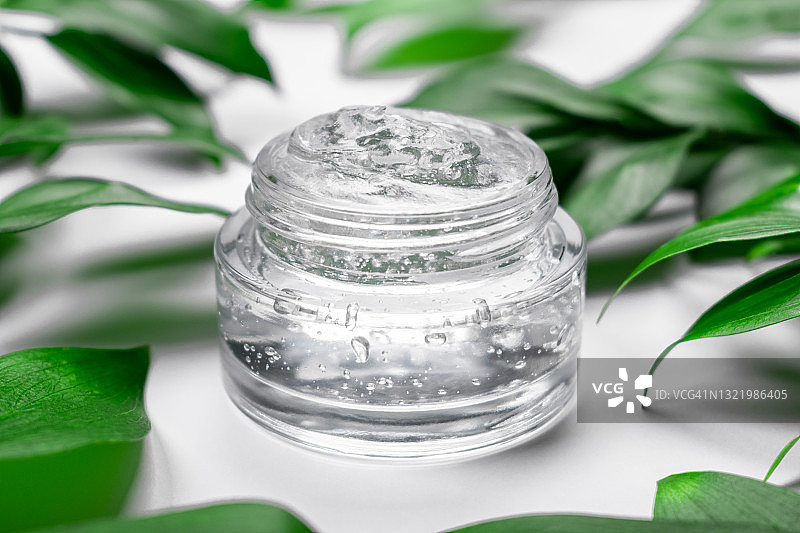 带有绿叶的白色背景上的清透保湿精华、发胶、面部精华液罐，用于皮肤护理和化妆的化妆品图片素材