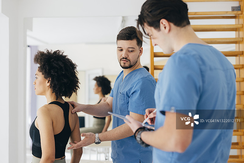 理疗师检查患者背部，同时同事准备报告图片素材