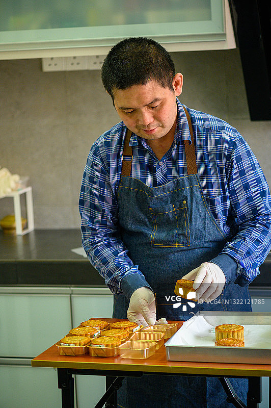 亚洲男面包师将自制的中式月饼放在金色塑料容器中图片素材