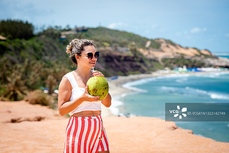 在海滩上看着风景，喝着椰子汁的漂亮女人图片素材